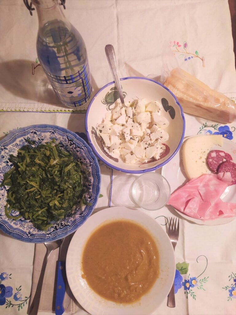 Italian dinner with soup, cold meats, mozzarella cheese, vegetables, parmesan cheese and a bottle of water