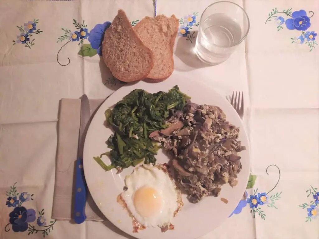 Fried eggs with a side of mushrooms and vegetables, two slices of bread and a glass of water